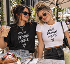 Two women wearing custom NXTBIAS T-shirts with “Your Design Here” graphics while enjoying brunch at an outdoor café.