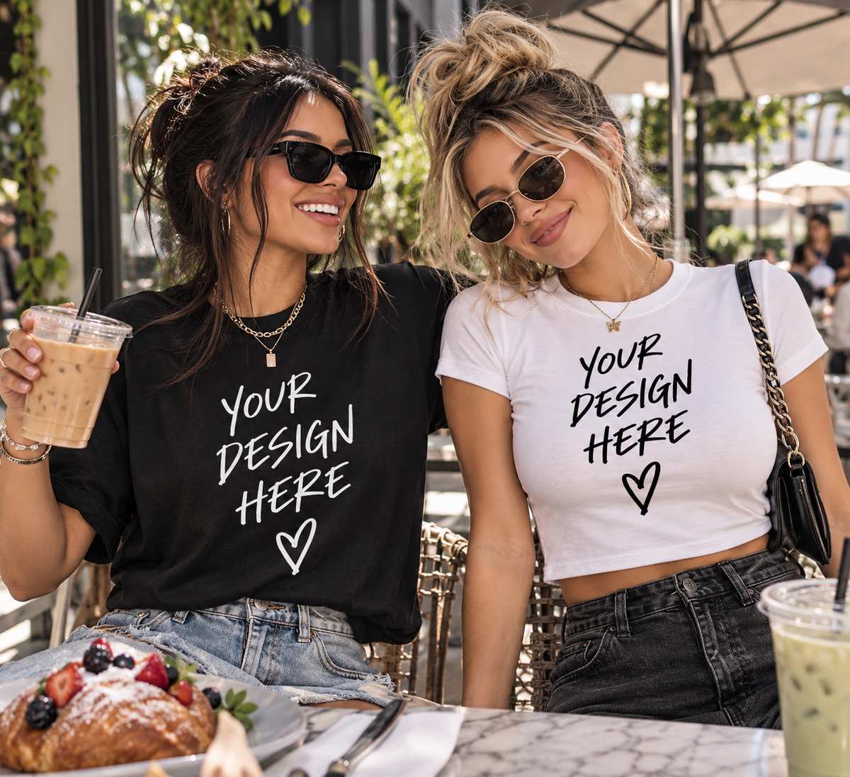 Two women wearing custom NXTBIAS T-shirts with “Your Design Here” graphics while enjoying brunch at an outdoor café.